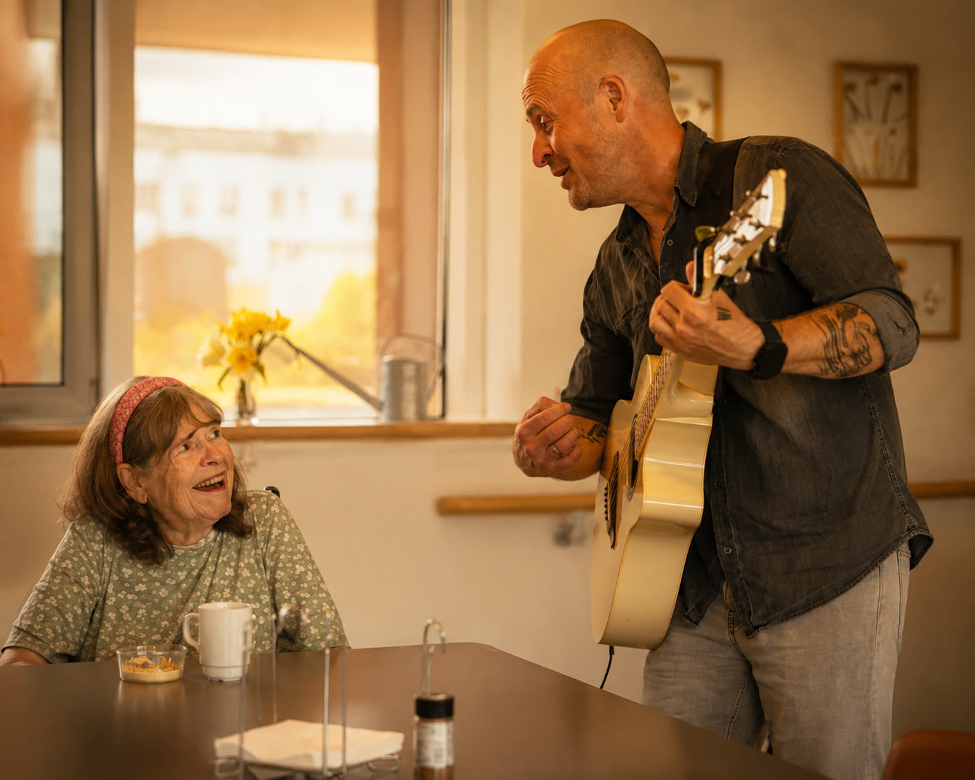 Klavs synger og spiller guitar tæt ved en ældre kvinde i en lys opholdsstue